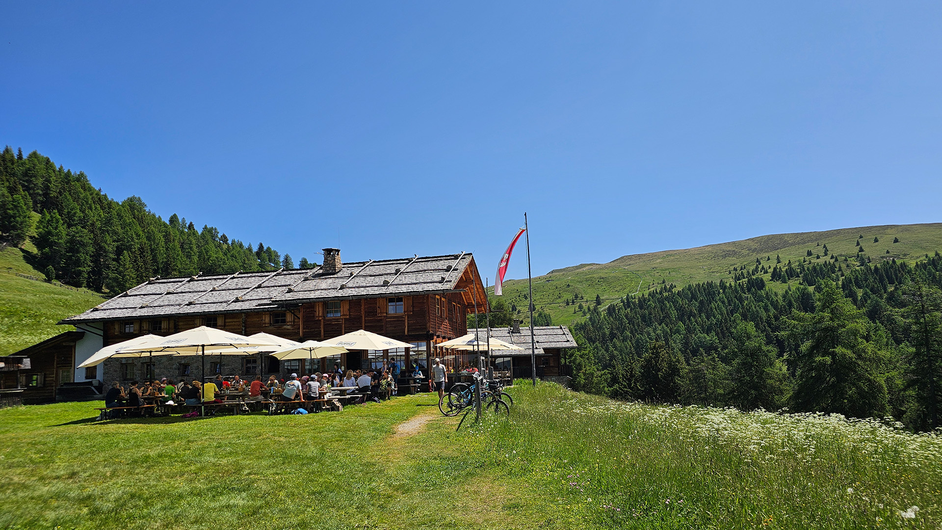 Berghütte, davor Tische und eine wehende Südtirol-Fahne