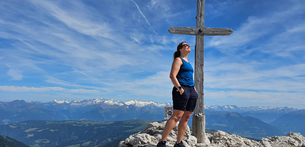 Frau steht bei Gipfelkreuz auf Berggipfel