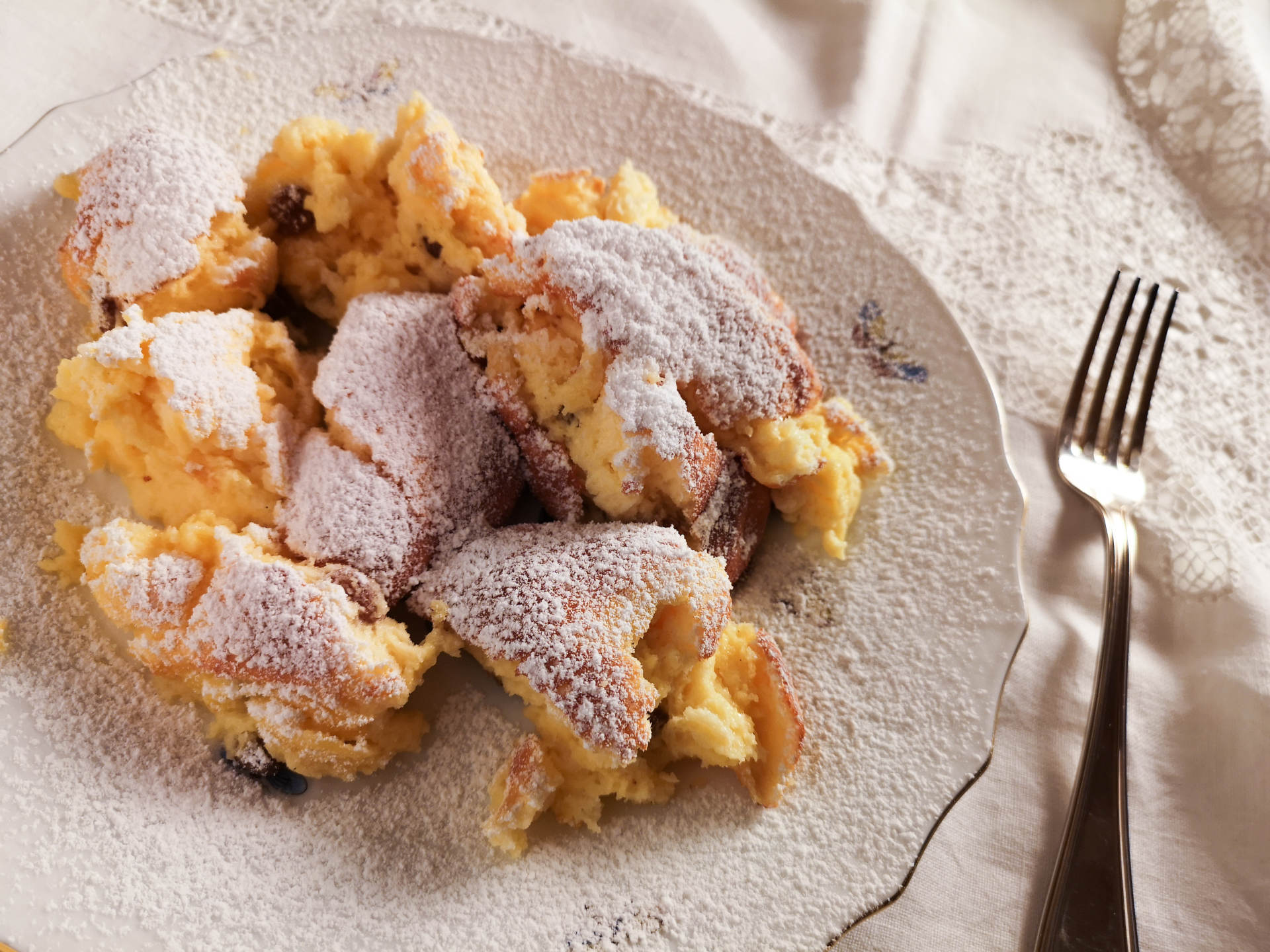Gebackener Topfenschmarren mit Staubzucker bestreut und weißem Teller mit Tischtuch