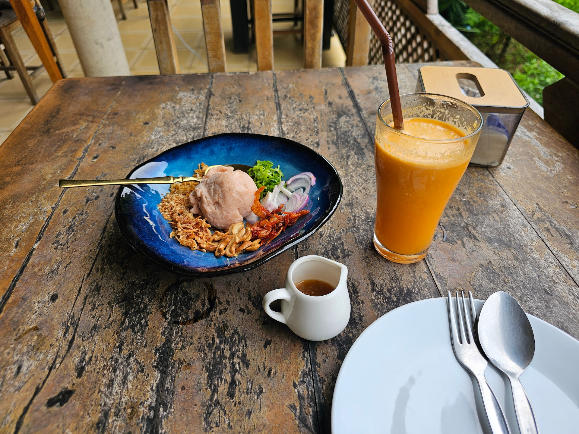Holztisch, darauf frischgepresster Saft, ein Suppenteller mit Salat und ein Kännchen mit Dressing