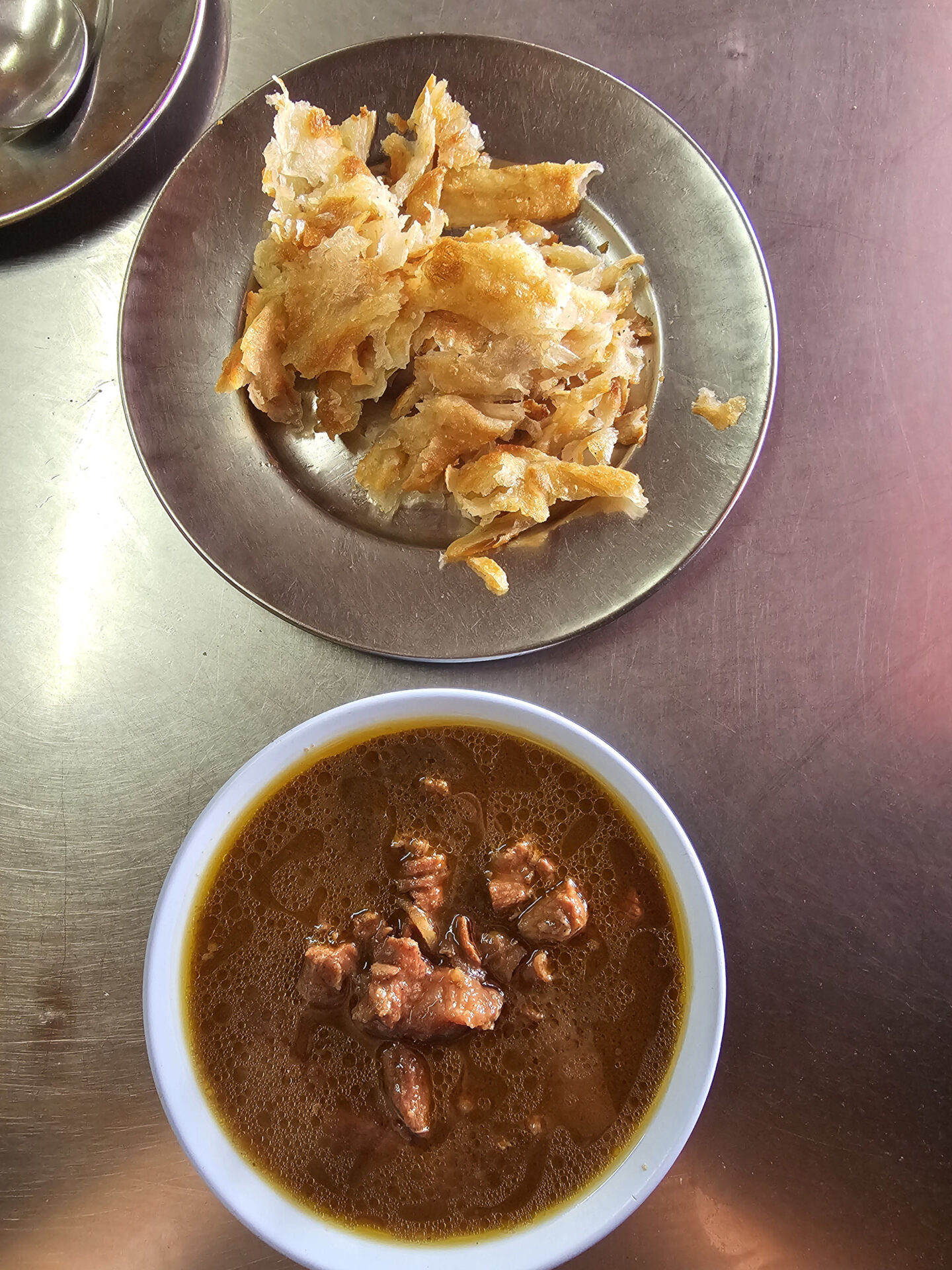 Ein silberner Teller mit zerrupftem Fladenbrot, darunter ein Schüsselchen Beef Curry