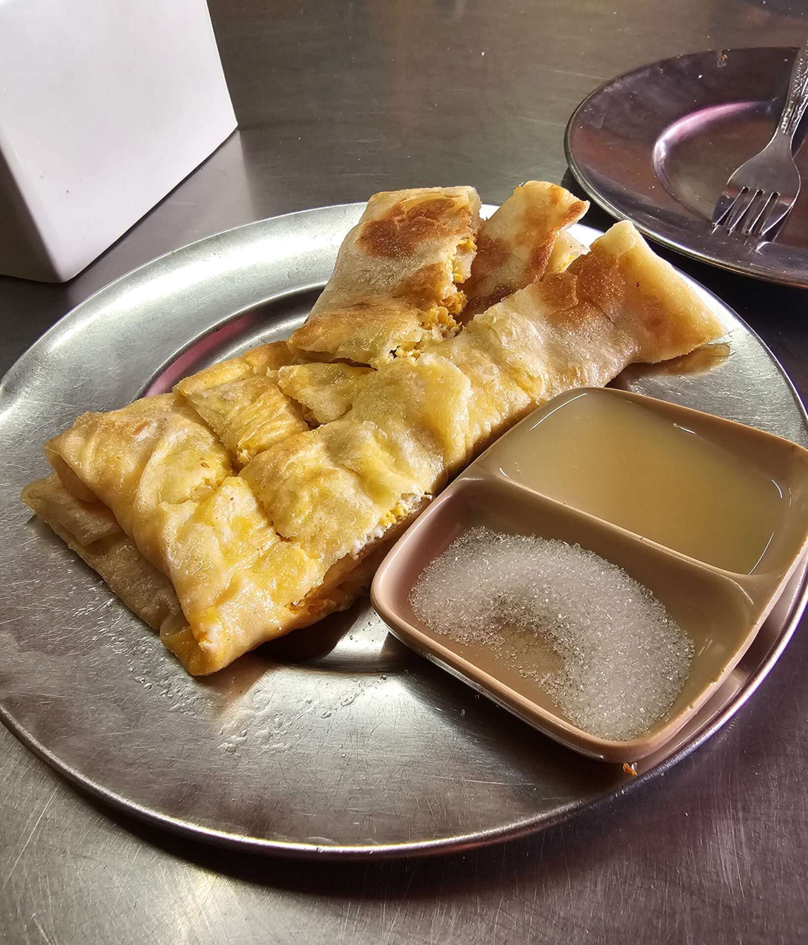 Gefüllter Fladen auf silbernem Teller, dazu ein Schüsselchen mit Zucker und Kondensmilch